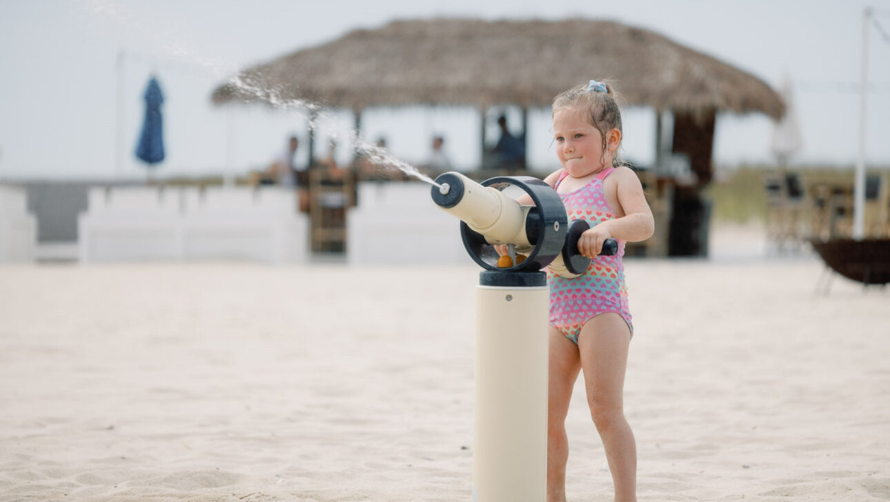 A girl playing with a water canon at a beach.