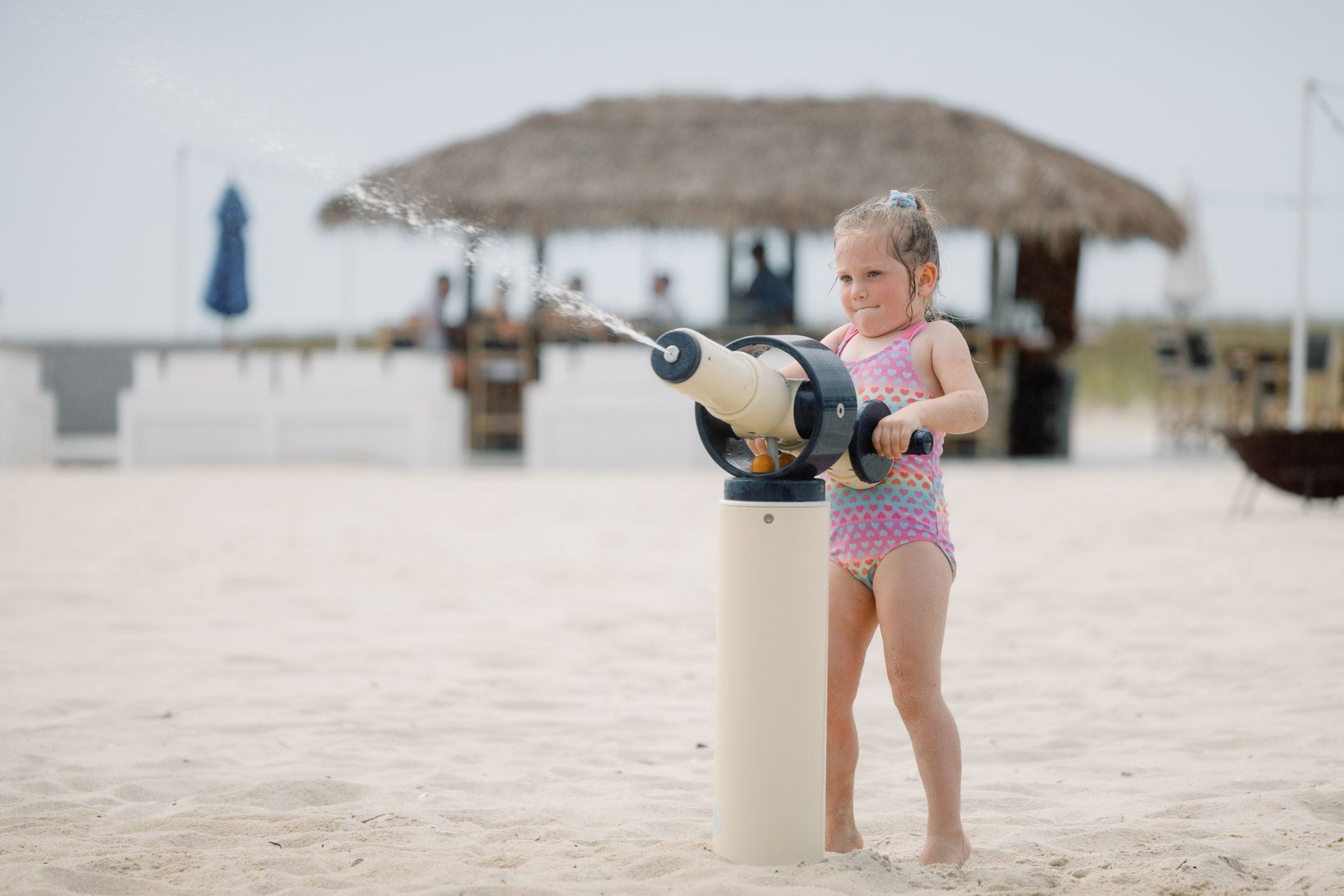 A girl playing with a water canon at a beach.