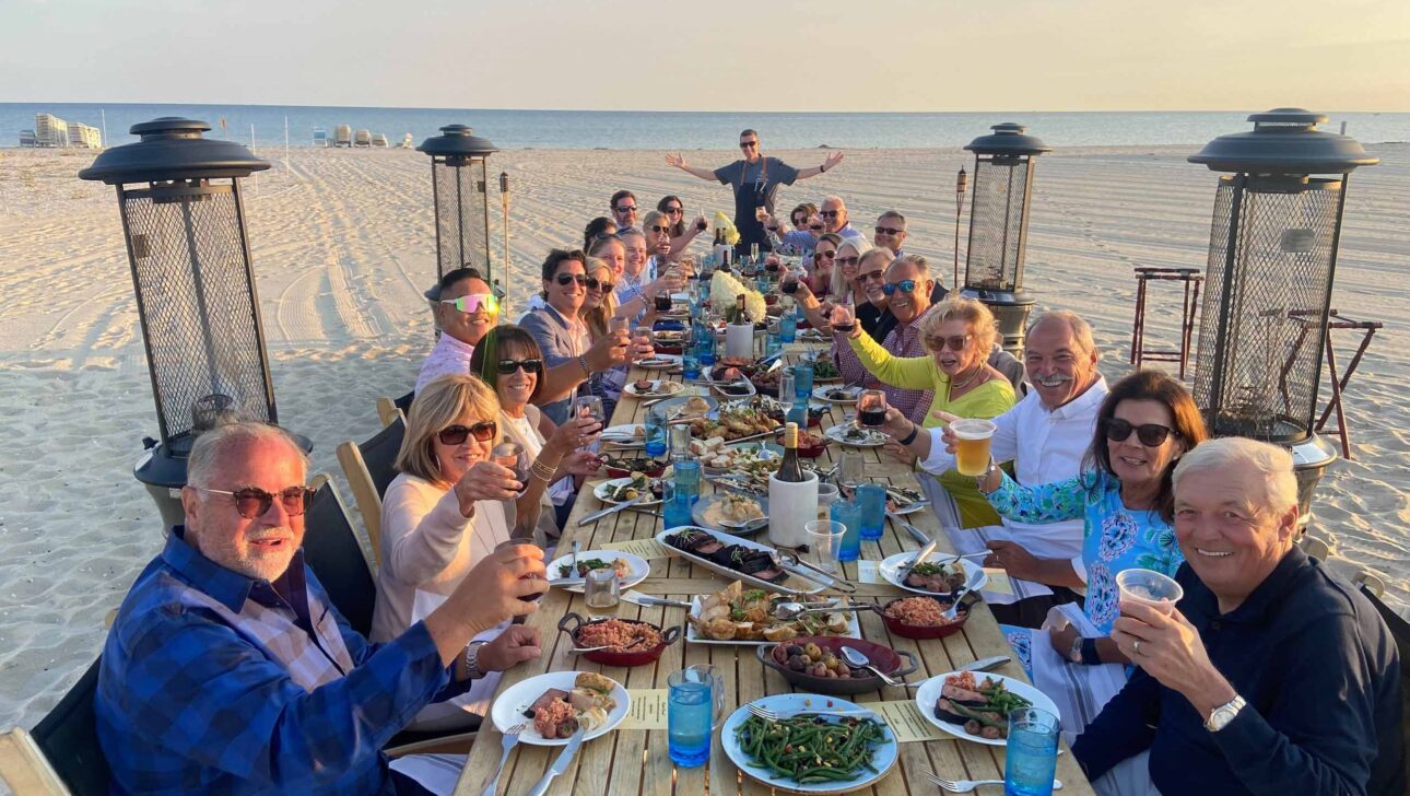 Family and friends gathered together for a meal on a beach.